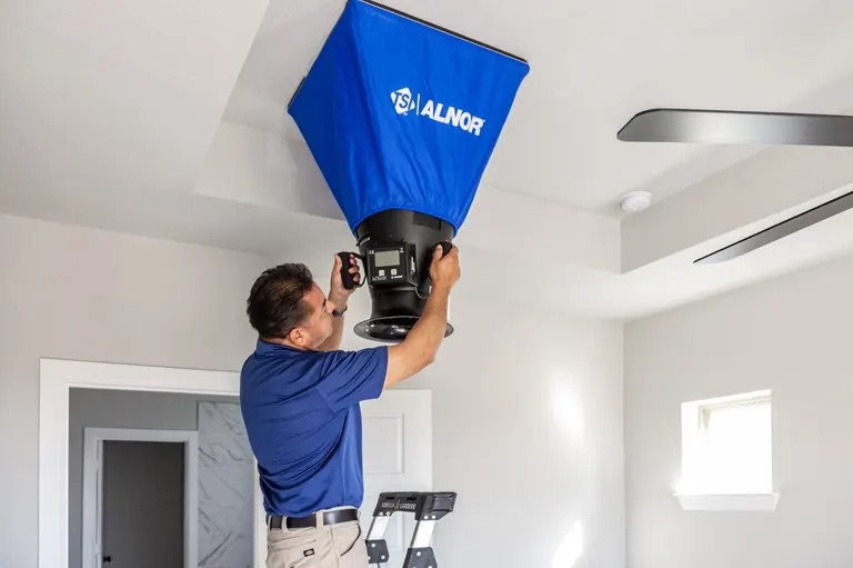 A HERS rater running a duct leakage test with a duct blaster